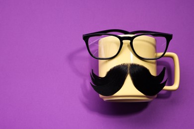 Man's face made of artificial mustache, cup and glasses on purple background, top view. Space for text