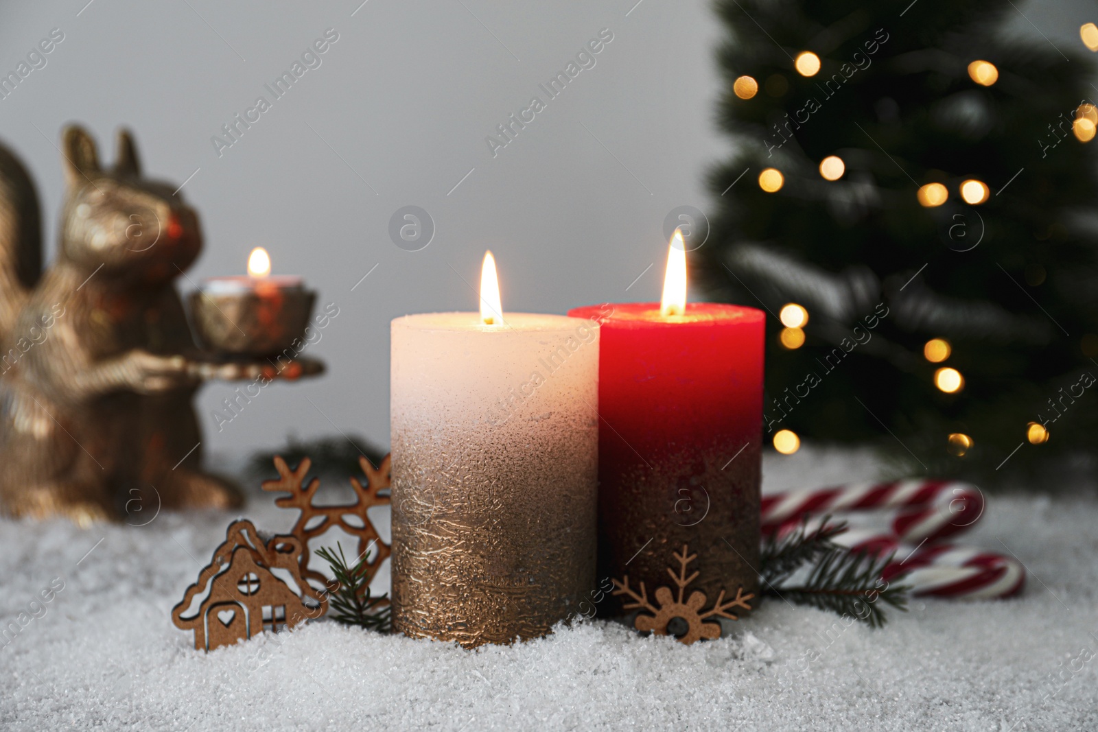 Photo of Burning candles and Christmas decor on artificial snow