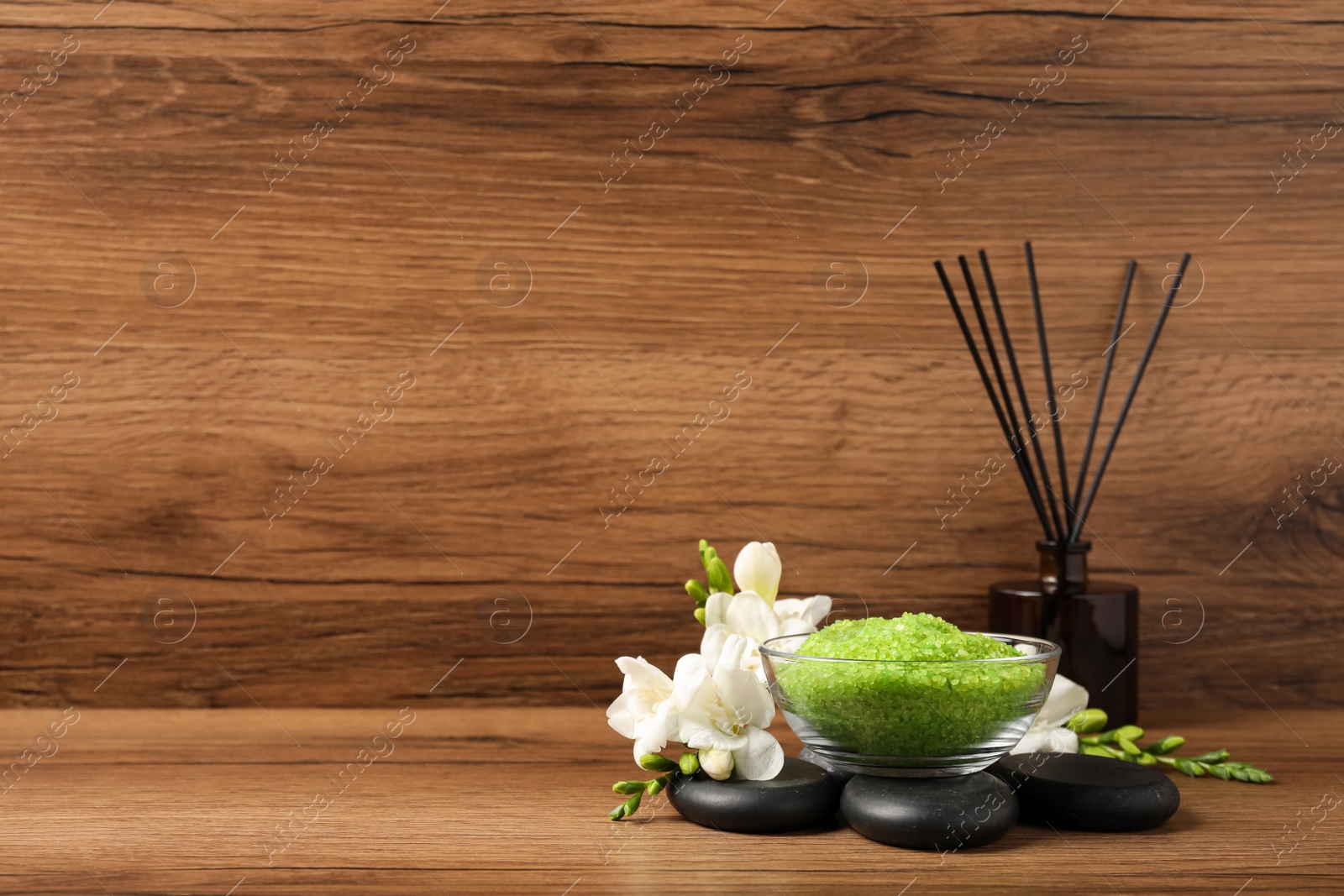 Photo of Aromatic sea salt, flowers and spa stones on wooden table, space for text