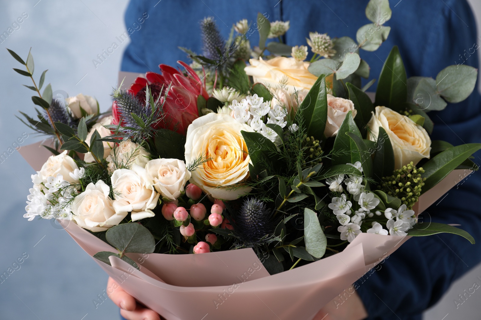 Photo of Woman with bouquet of beautiful roses on light blue background, closeup