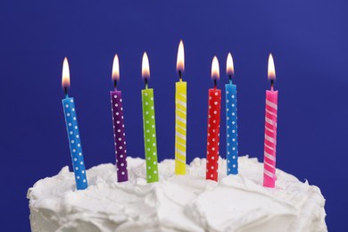 Delicious cake with cream and burning candles on blue background, closeup