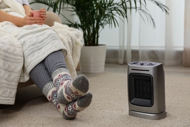 Woman warming legs near halogen heater at home, closeup