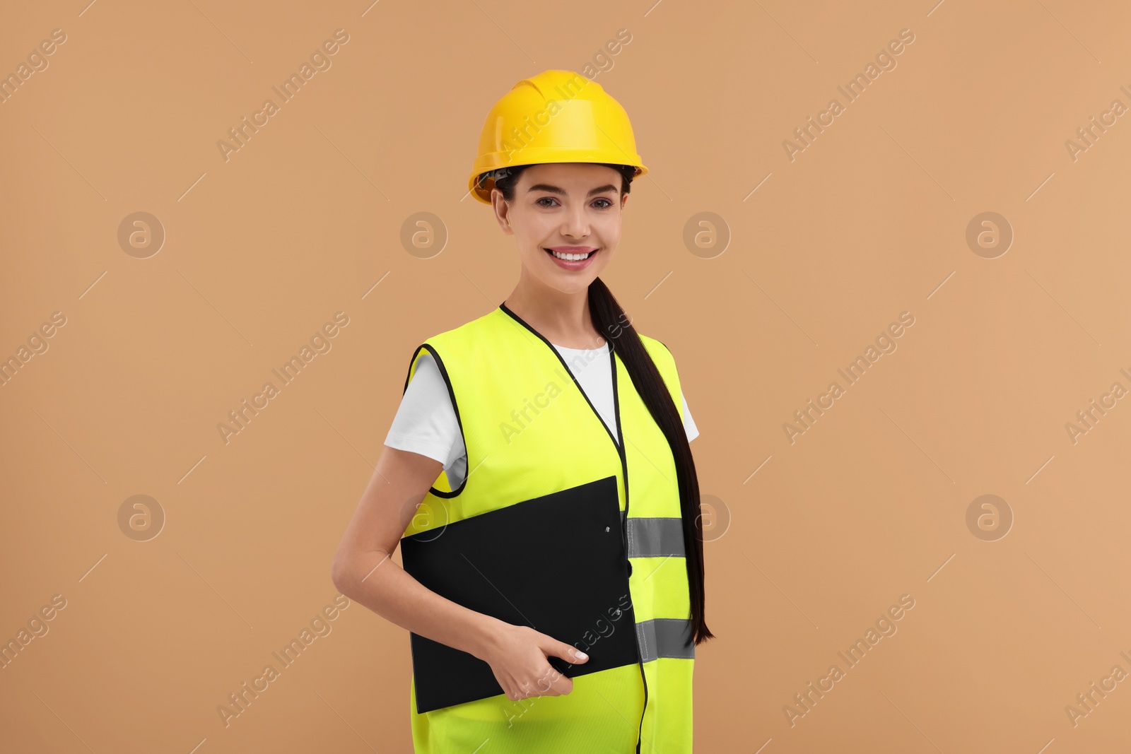 Photo of Engineer in hard hat holding clipboard on beige background