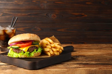 Delicious burger, soda drink and french fries served on wooden table. Space for text