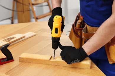 Photo of Young worker using electric drill at table in workshop, closeup