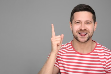 Happy man showing his tongue and pointing at something on grey background. Space for text