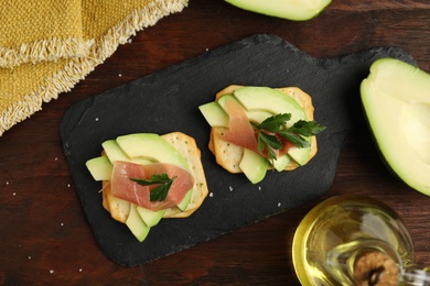 Photo of Delicious crackers with avocado, prosciutto and parsley on wooden table, flat lay