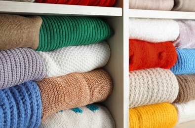 Folded colorful winter sweaters on shelves as background