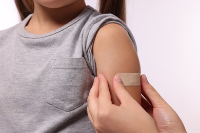 Photo of Woman sticking plaster on girl's arm after vaccination against white background, closeup