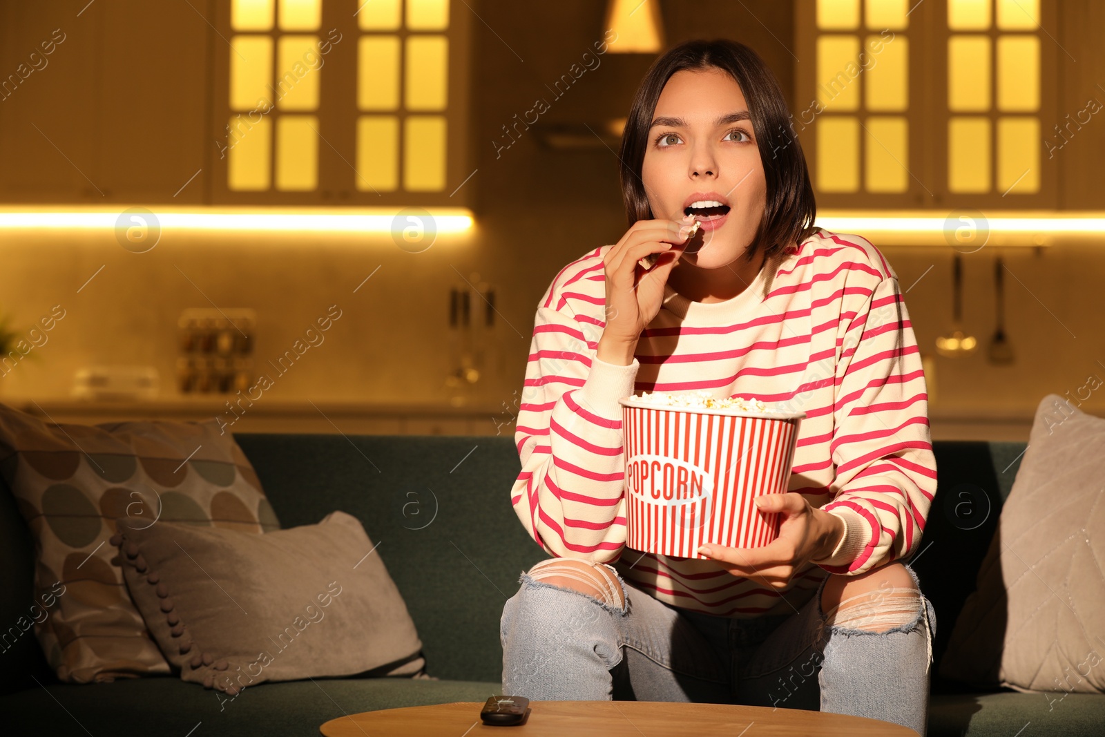 Photo of Surprised woman eating popcorn while watching TV on sofa at home, space for text