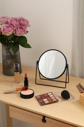 Photo of Mirror, cosmetic products and vase with pink roses on wooden dressing table in makeup room