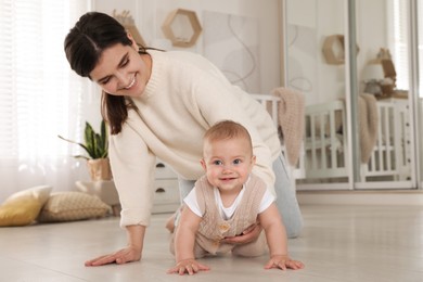 Photo of Happy young mother helping her cute baby to crawl on floor at home