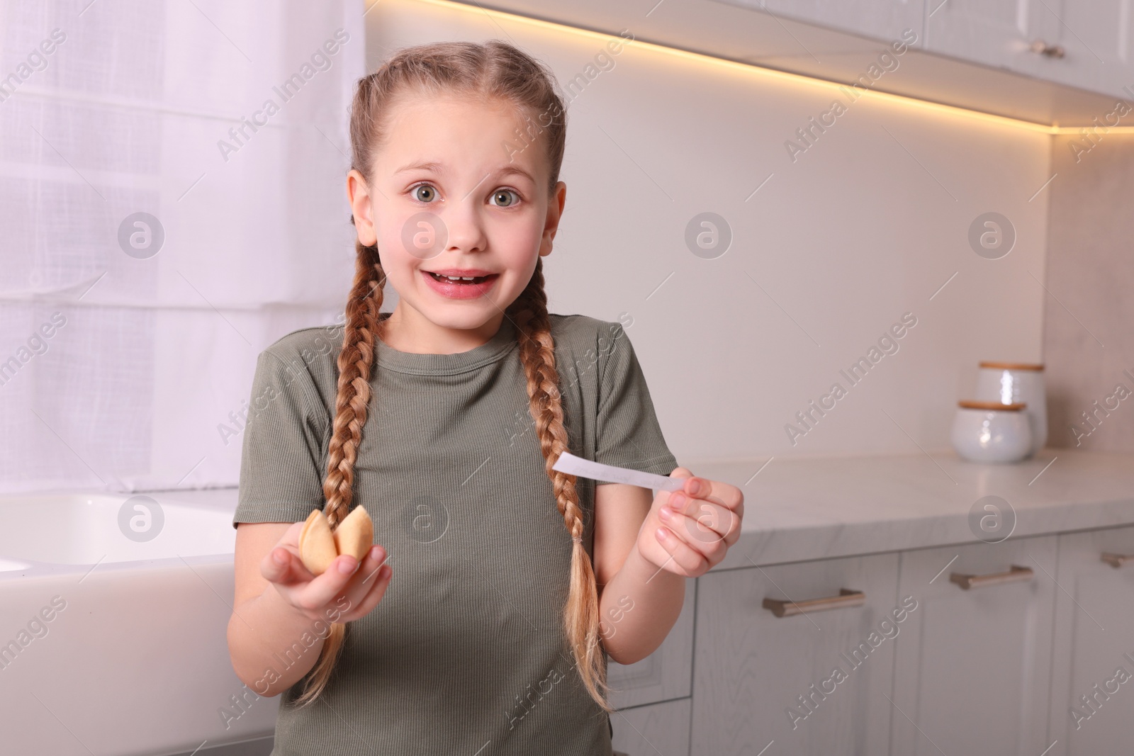 Photo of Cute girl holding tasty fortune cookie and reading prediction indoors. Space for text