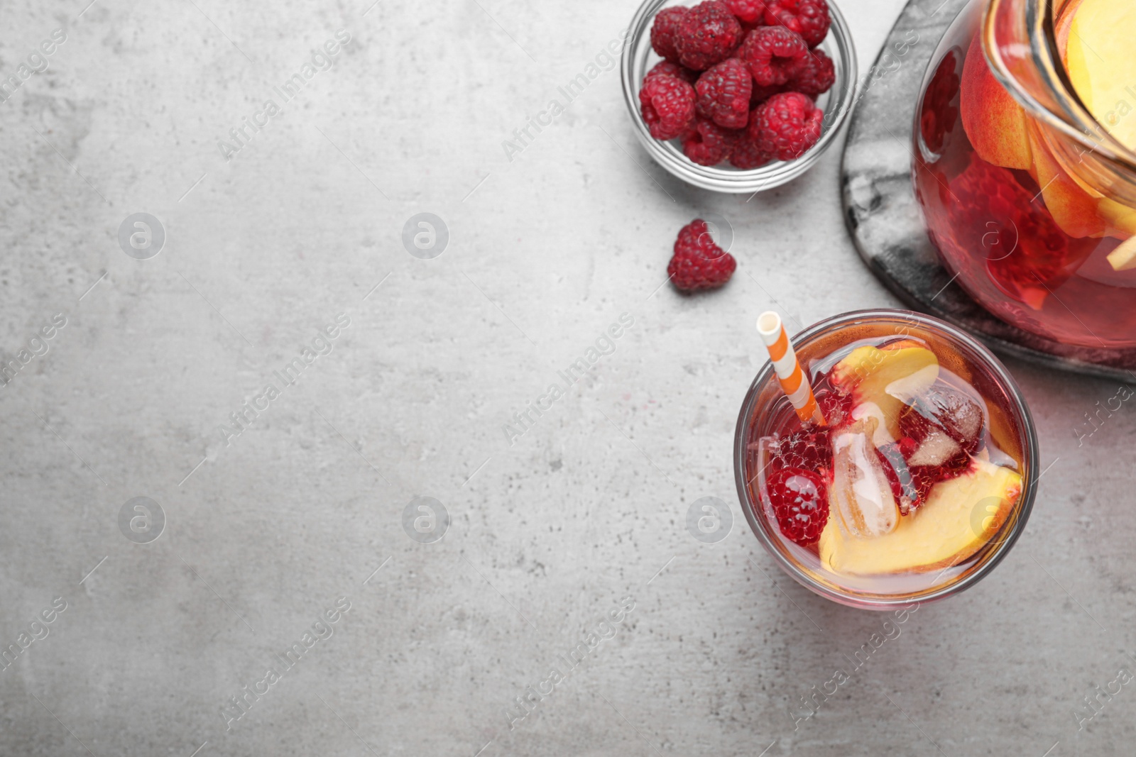 Photo of Flat lay composition of delicious peach lemonade with soda water and raspberries on grey table, space for text. Fresh summer cocktail