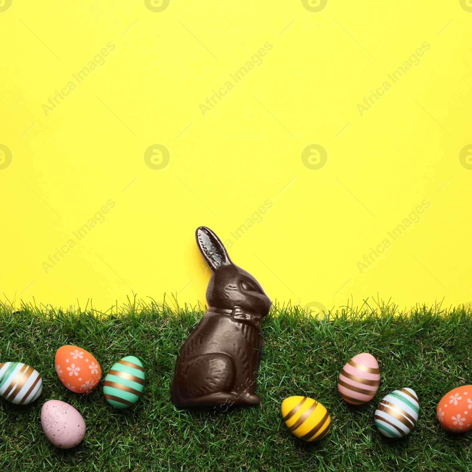 Photo of Chocolate Easter bunny and eggs with green grass on yellow background