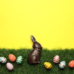 Chocolate Easter bunny and eggs with green grass on yellow background