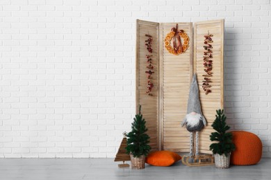 Photo of Beautiful Christmas themed photo zone with small trees, dwarf and fir decor near white brick wall. Space for text