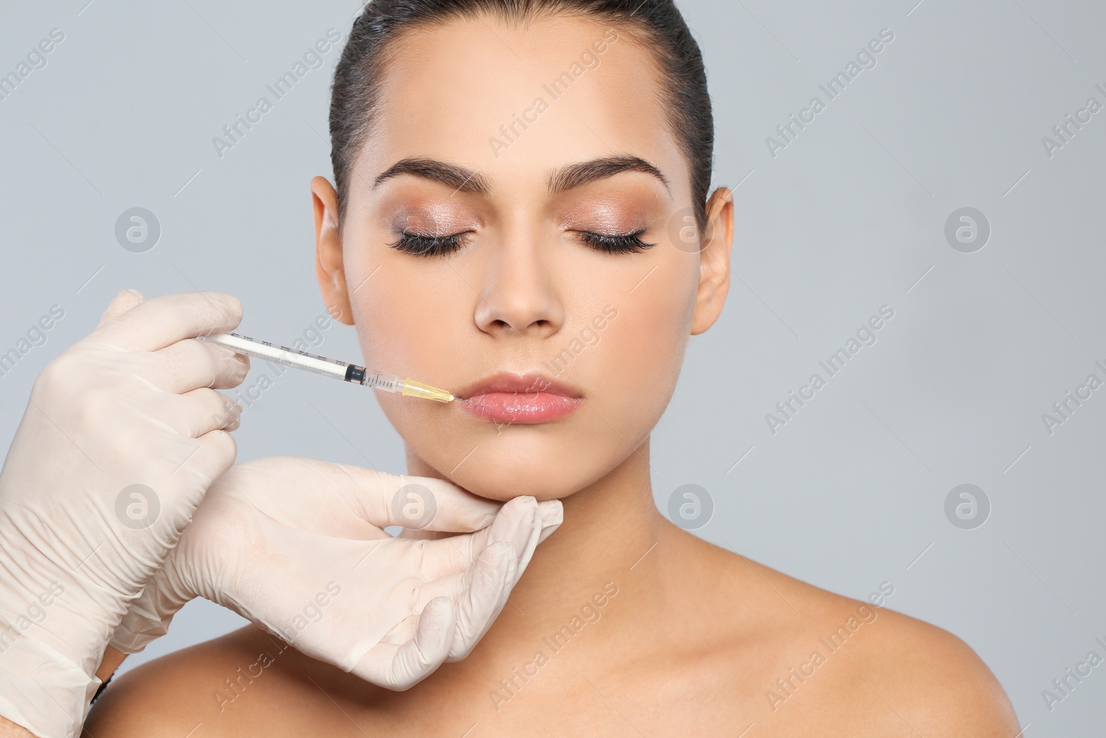 Photo of Young woman getting lips injection on grey background. Cosmetic surgery