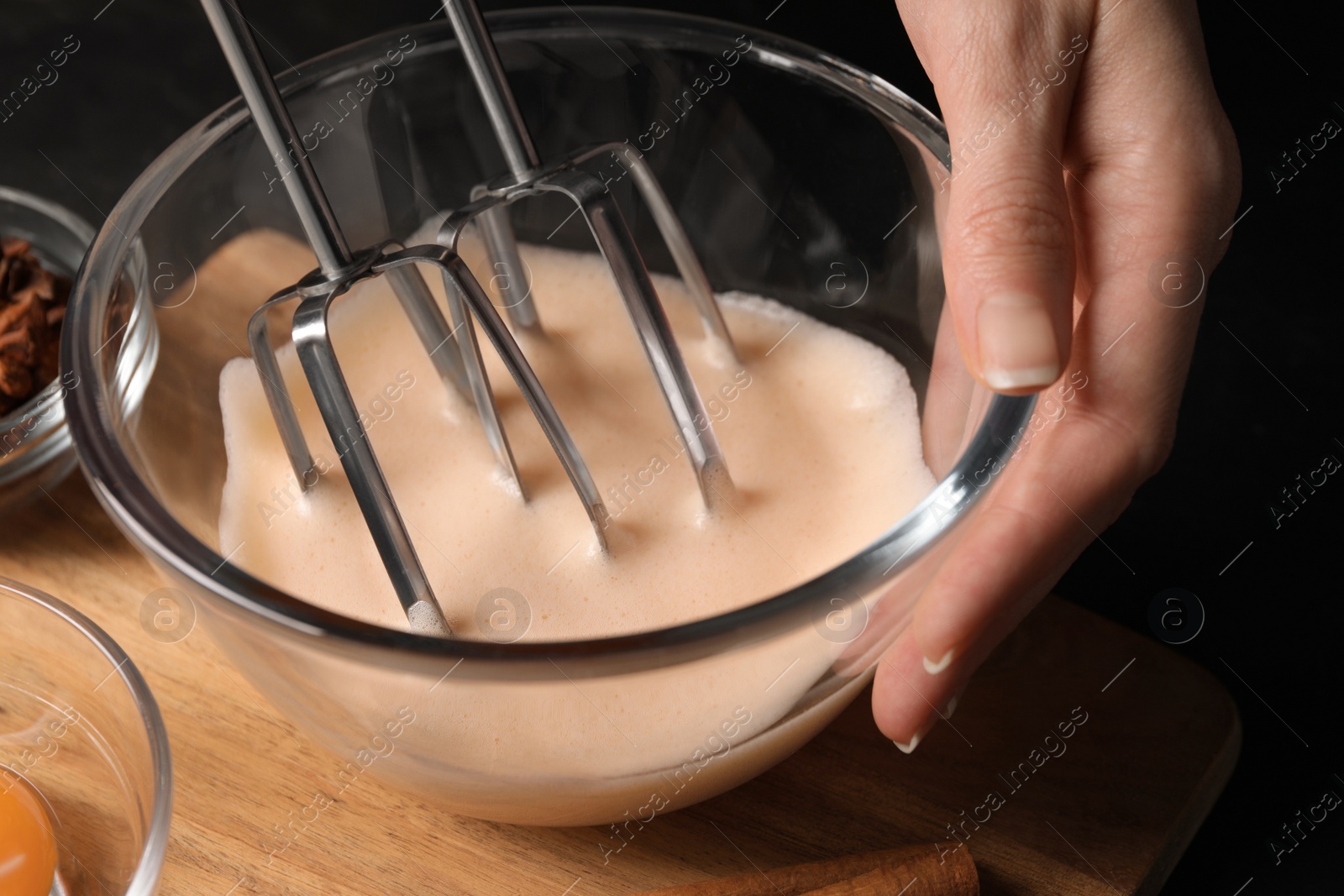 Photo of Woman whipping ingredients with mixer at black table, closeup. Cooking delicious eggnog