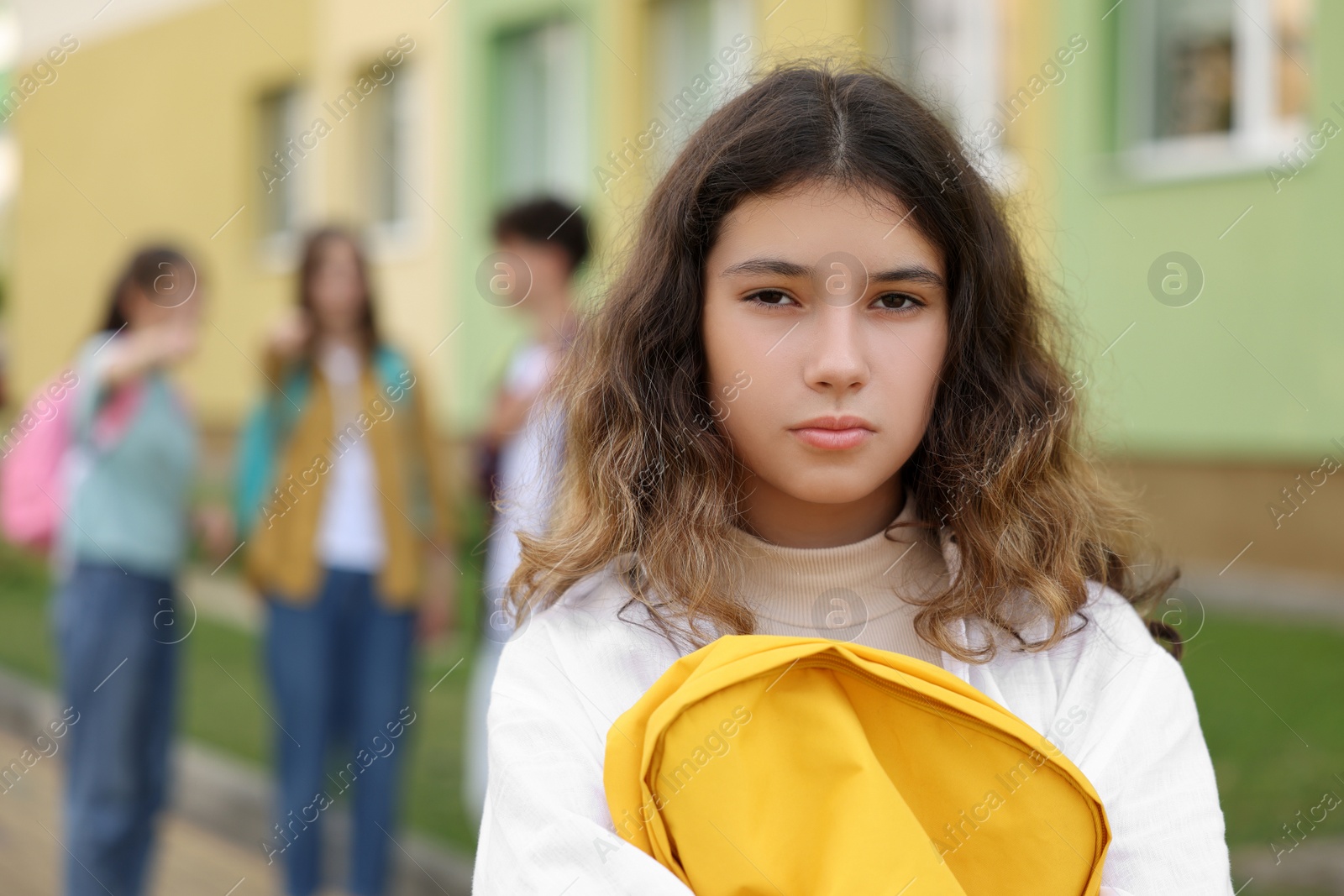 Photo of Teen problems. Lonely girl standing separately from other students outdoors