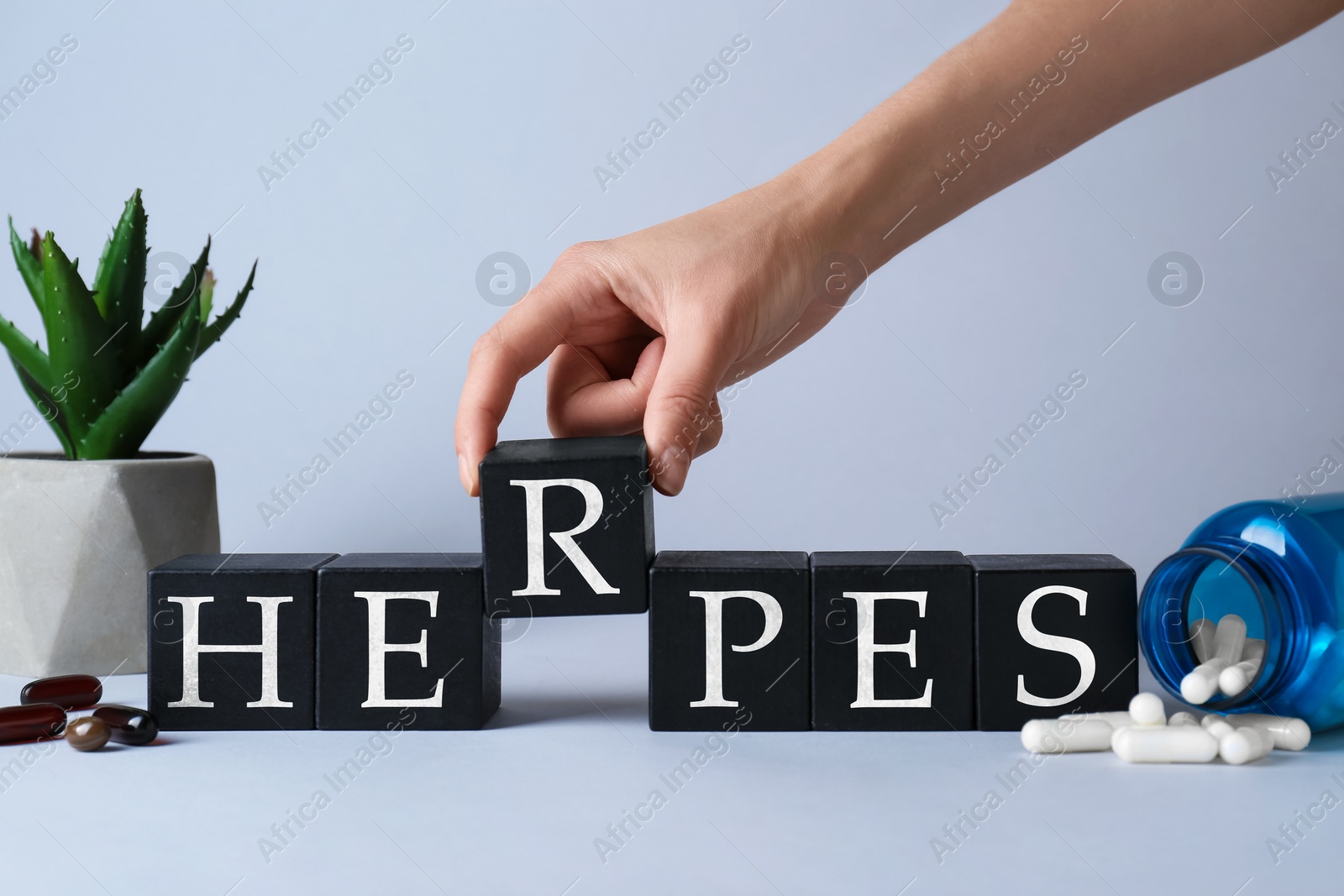 Photo of Woman making word Herpes with wooden cubes at grey table, closeup