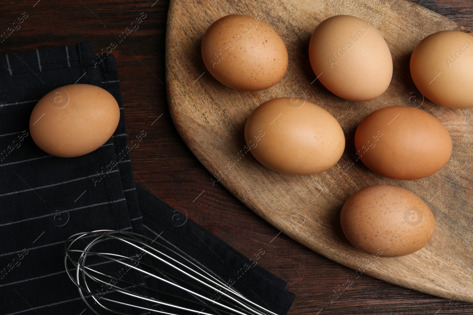 Photo of Chicken eggs and whisk on wooden table, flat lay