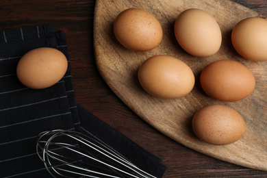 Photo of Chicken eggs and whisk on wooden table, flat lay