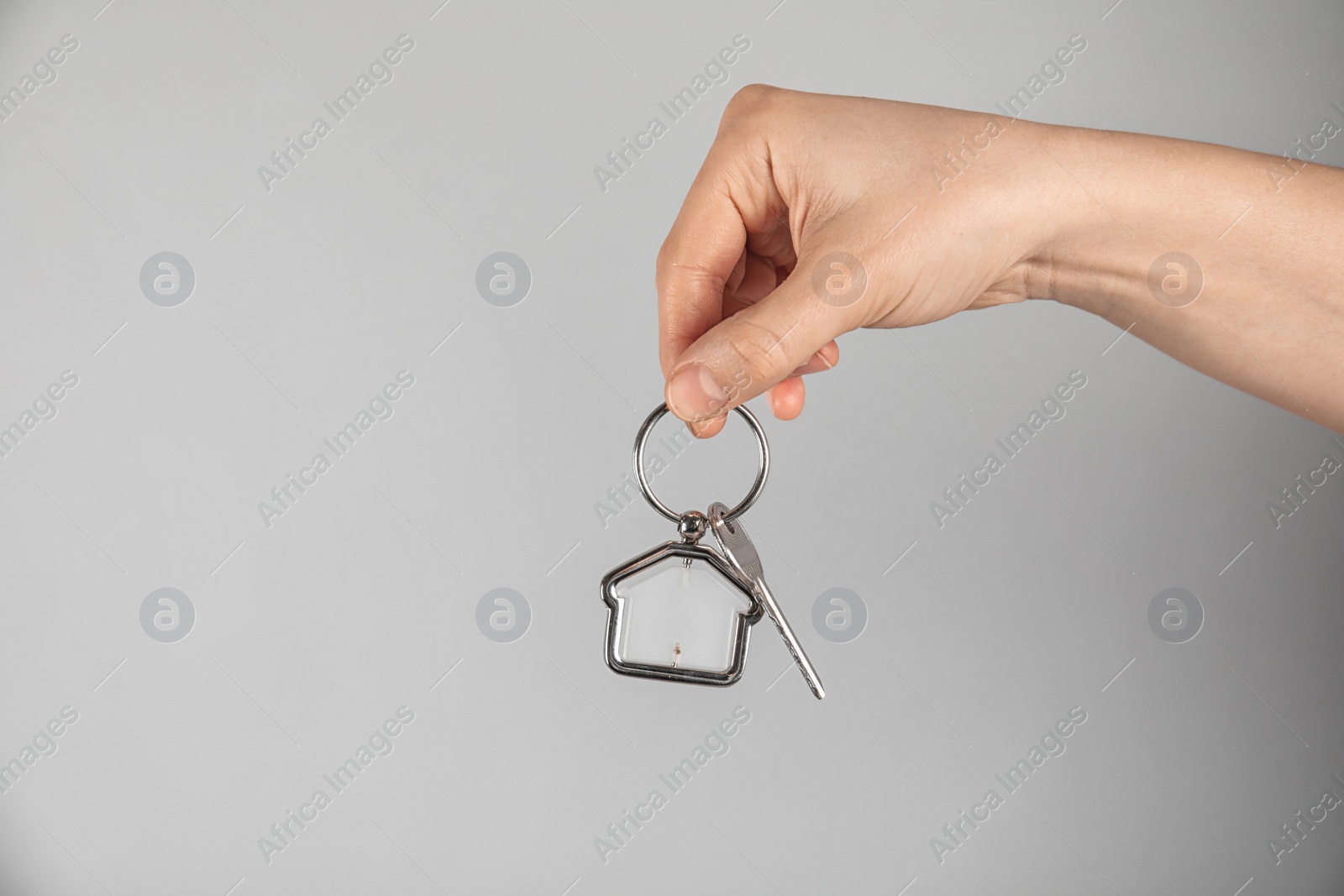 Photo of Young woman holding house key with trinket on grey background, closeup. Space for text