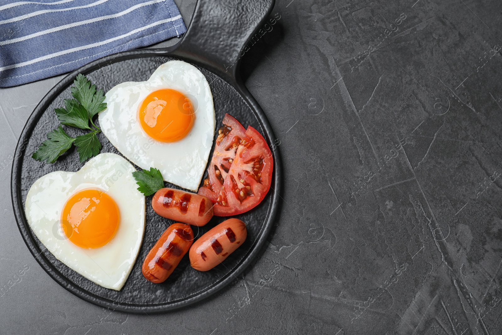 Photo of Delicious breakfast with heart shaped fried eggs and  sausages served on dark grey table, flat lay. Space for text