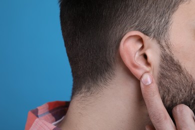 Photo of Man pointing at his ear on light blue background, closeup