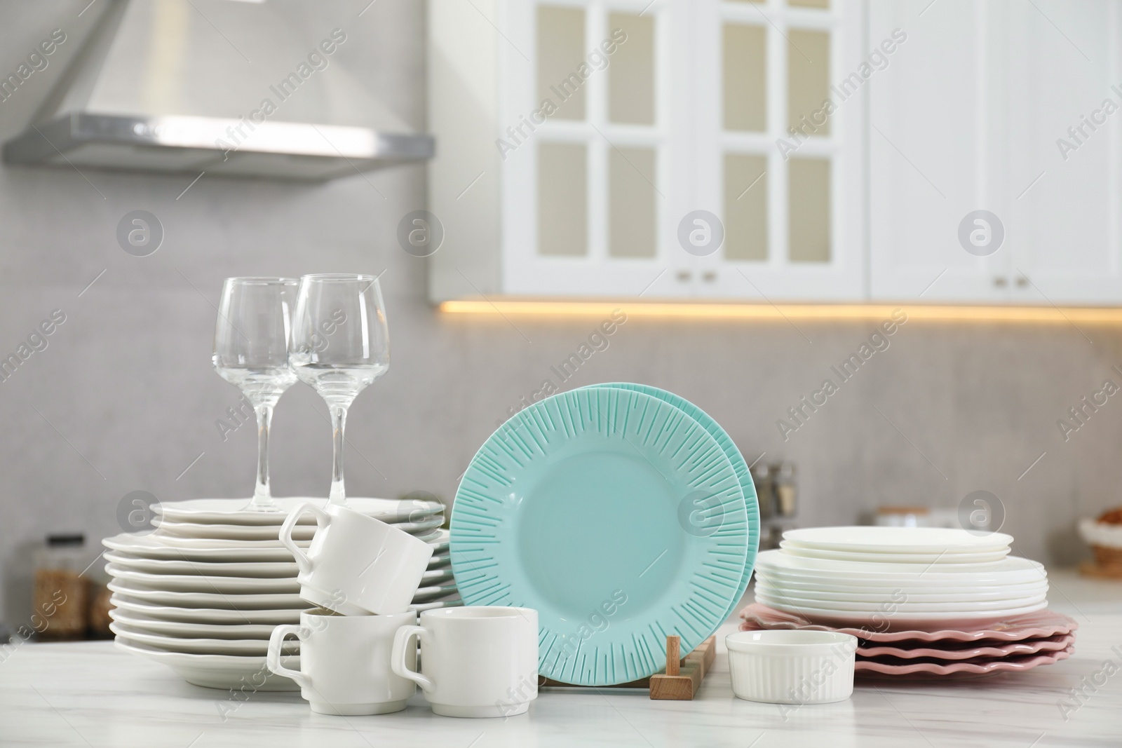 Photo of Clean plates, cups, glasses and bowl on white marble table in kitchen