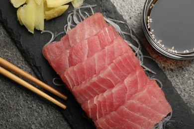 Tasty sashimi (pieces of fresh raw tuna), glass noodles, soy sauce and chopsticks on gray table, flat lay