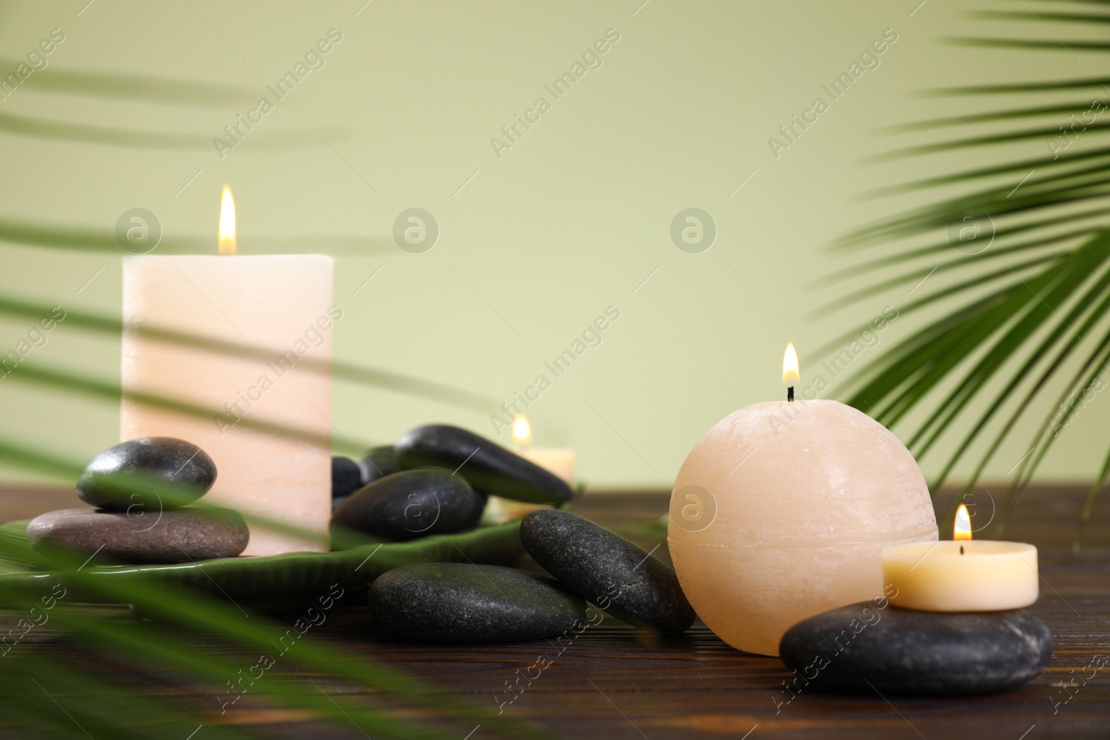 Photo of Composition of spa stones and burning candles on wooden table against light green background