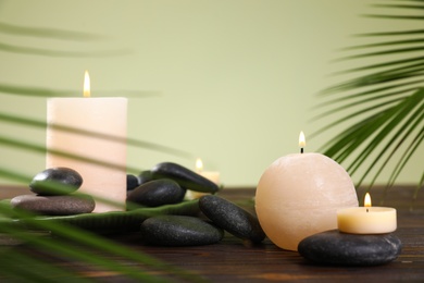 Composition of spa stones and burning candles on wooden table against light green background