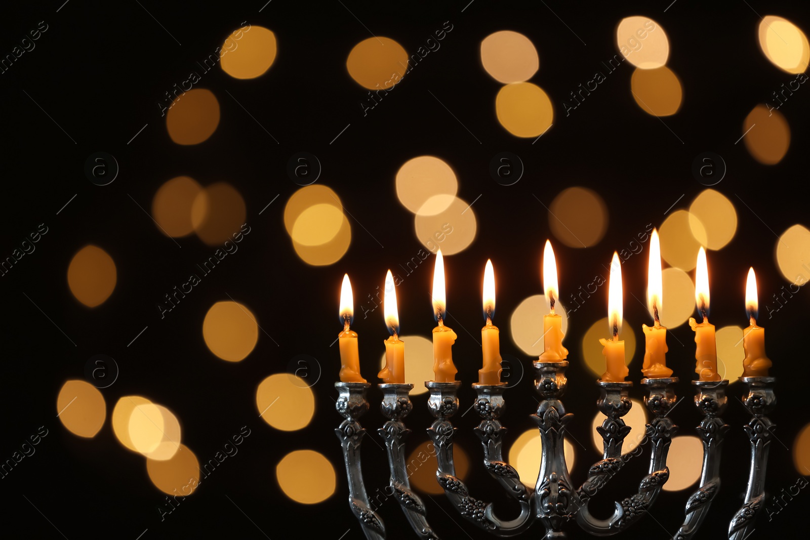 Photo of Silver menorah with burning candles against dark background and blurred festive lights, space for text. Hanukkah celebration