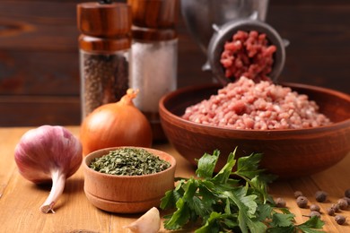 Photo of Manual meat grinder with beef mince, spices and parsley on wooden table, selective focus