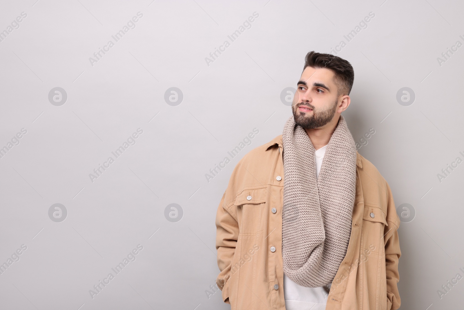 Photo of Handsome man in warm scarf on light grey background. Space for text