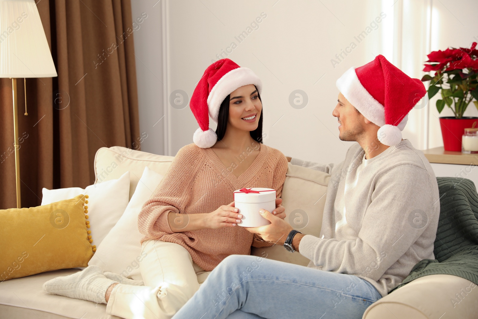 Photo of Happy young couple with Christmas gift sitting on sofa in living room