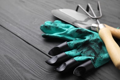 Photo of Gardening gloves, trowel and rake on grey wooden table, closeup. Space for text