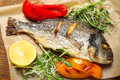 Photo of Delicious roasted fish and vegetables on wooden board, closeup