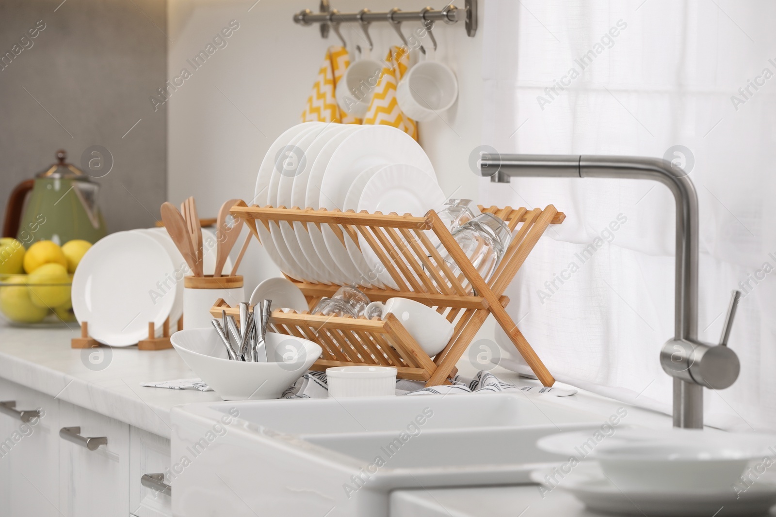 Photo of Sink and drying rack with clean dishes and cutlery on countertop in kitchen