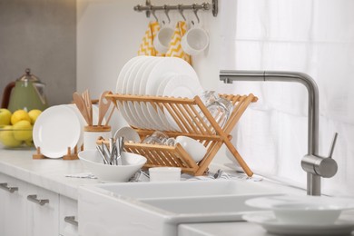 Photo of Sink and drying rack with clean dishes and cutlery on countertop in kitchen