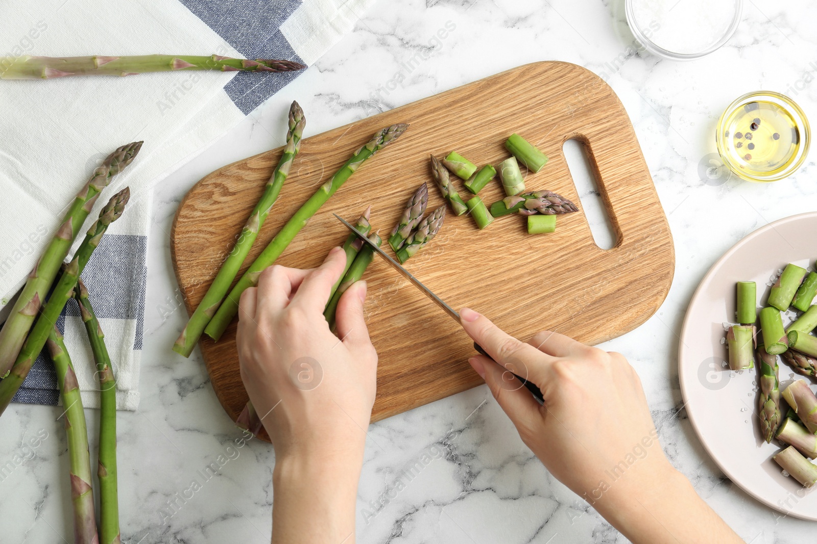 Photo of Woman cutting asparagus at white marble table, top view