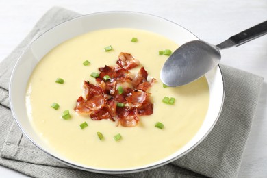 Photo of Tasty potato soup with bacon in bowl and spoon on white table