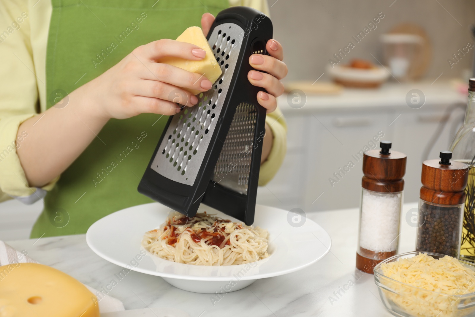 Photo of Woman grating cheese onto delicious pasta at white marble table in kitchen, closeup