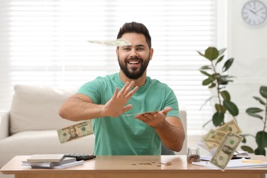 Photo of Happy young man throwing money at wooden table indoors