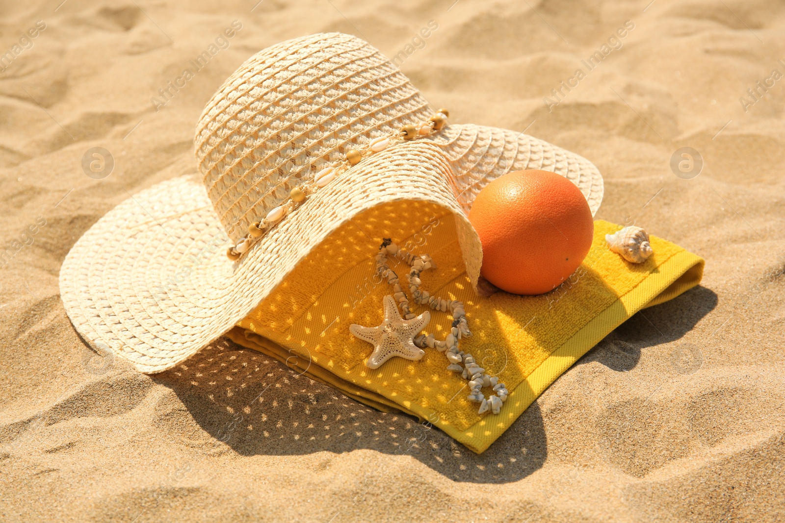 Photo of Straw hat, towel and orange on sand