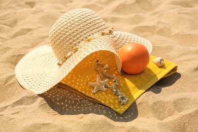 Straw hat, towel and orange on sand