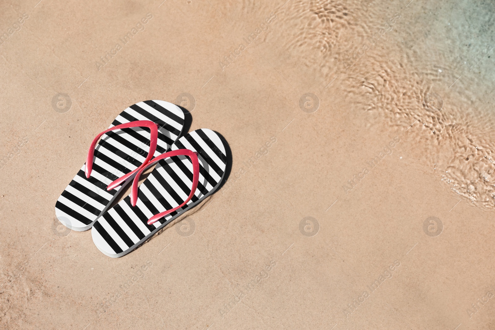 Photo of Stylish flip flops on sandy beach near sea, above view. Space for text