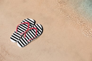 Photo of Stylish flip flops on sandy beach near sea, above view. Space for text